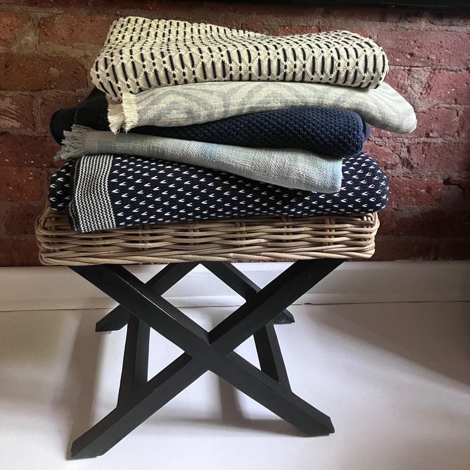 Foldable black stand with patterned throws against a brick wall.