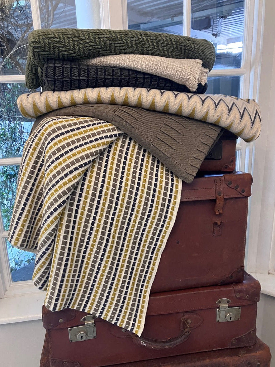 Stack of vintage suitcases with patterned throws on a windowsill