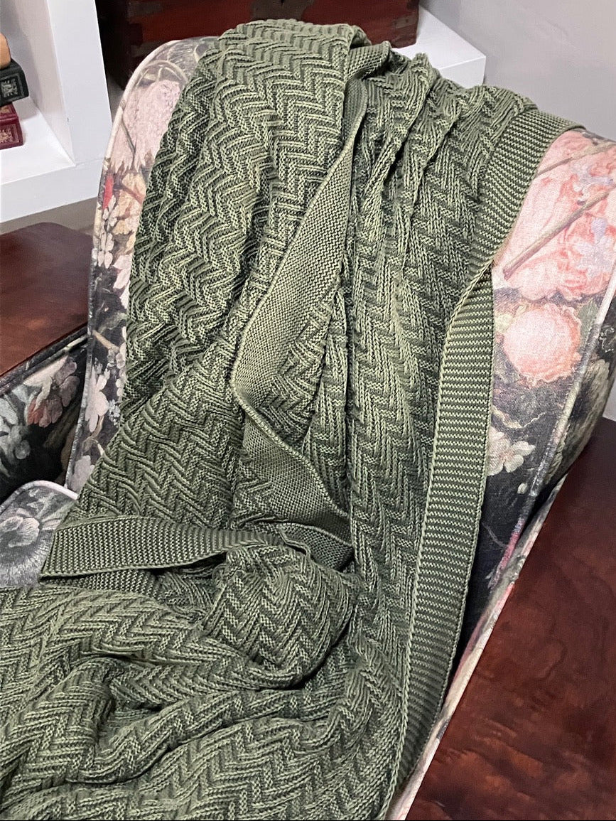 Green plain knitted throw on a floral-patterned and wooden chair