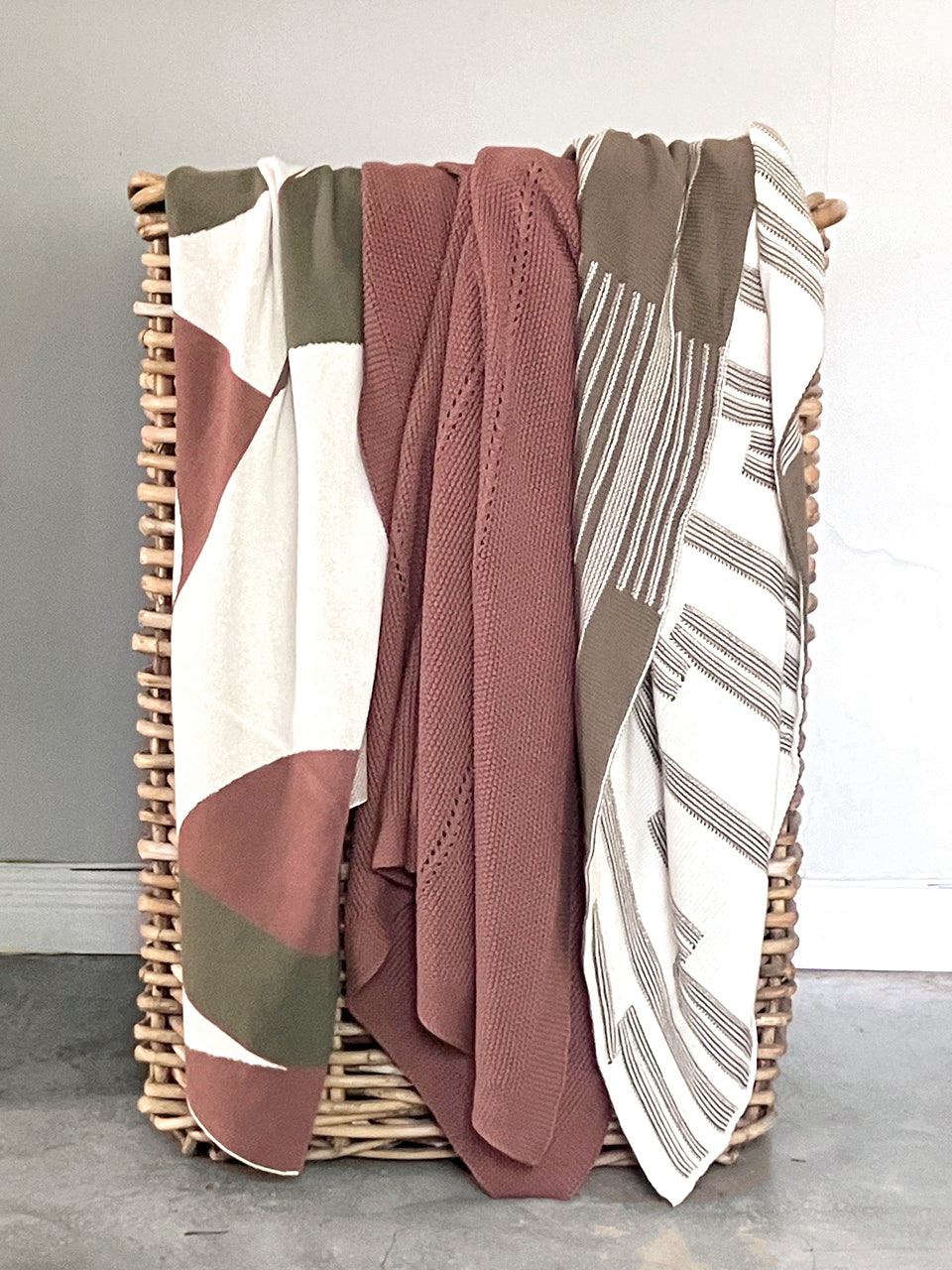 Wicker laundry basket filled with throws on a light gray floor.