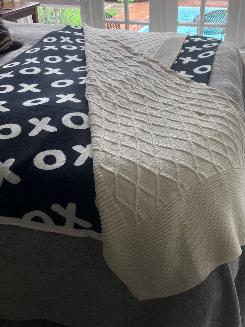 Beige knitted throw draped over a naughts and crosses patterned throw underneath.