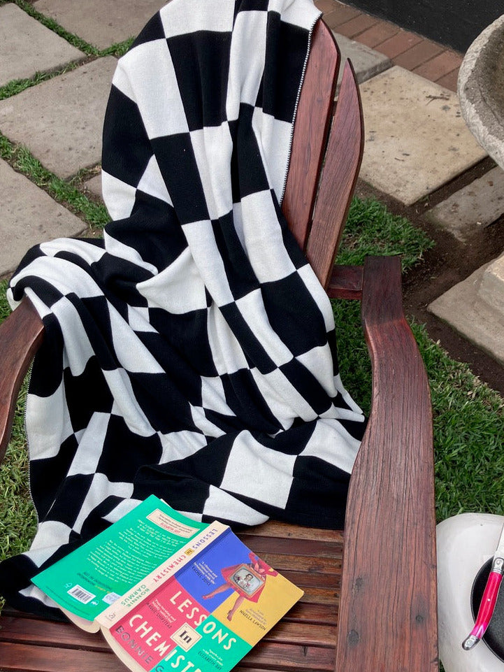 Black and white checkered throw on a wooden bench with books underneath, outdoors.